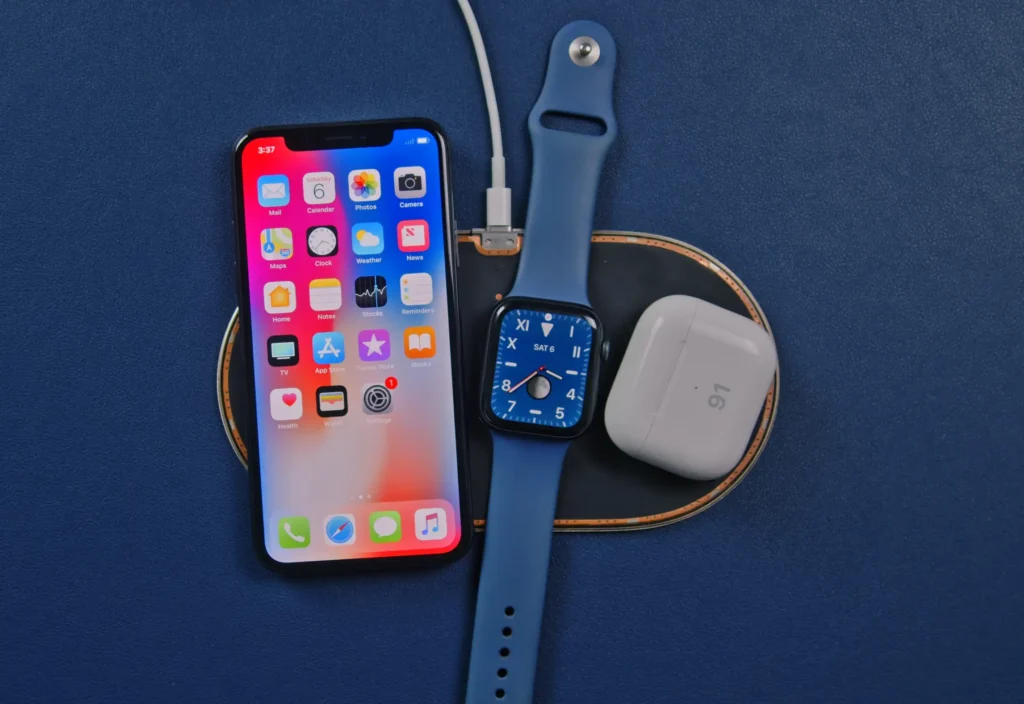 A contemporary Apple iPhone, Apple Watch, and AirPods charging wirelessly on a multi-device mat, representing modern tech alongside vintage failures.