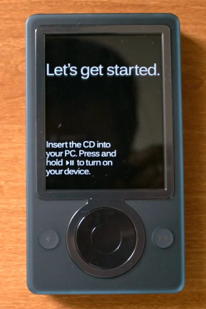 A brown Microsoft Zune 30 portable media player, showing its square control pad and a 'Let's get started' setup screen.